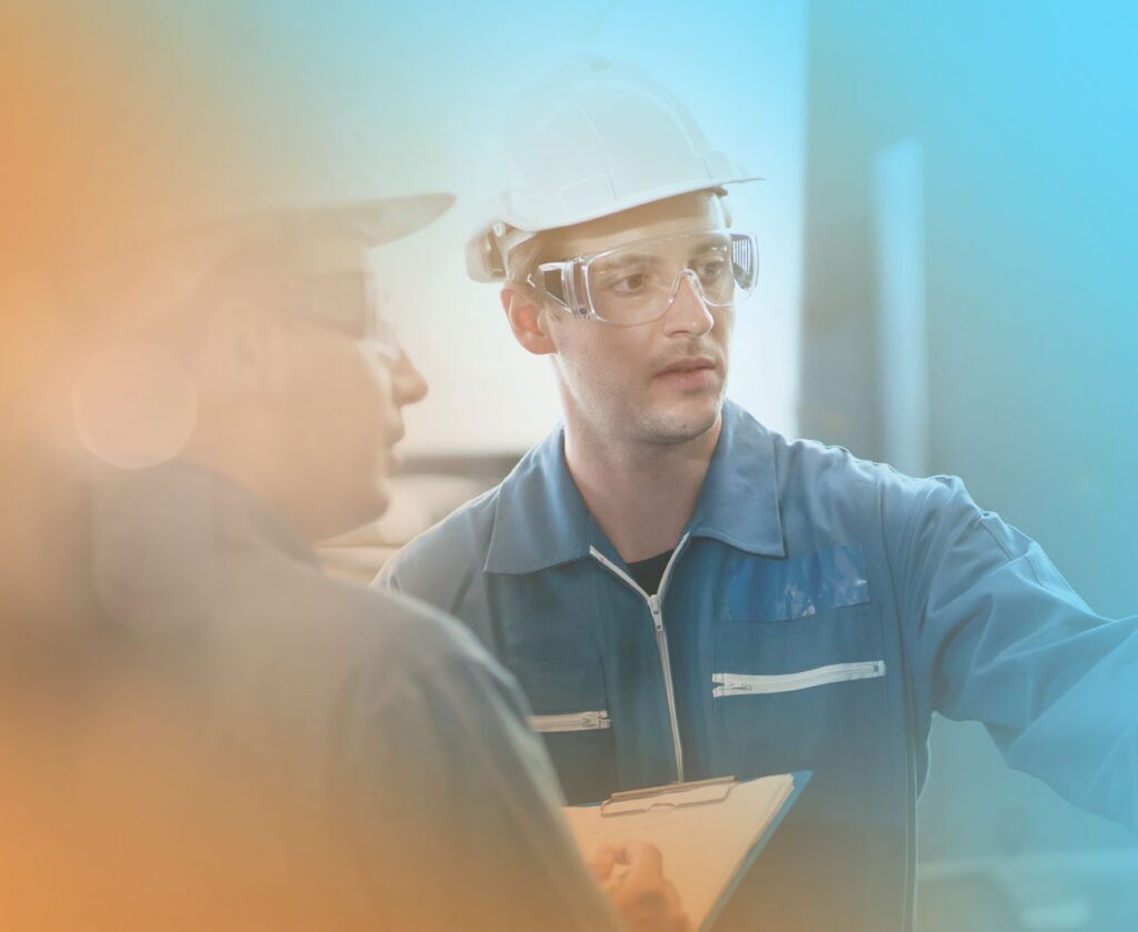 Two manufacturing employees wearing safety gear review information together on the production floor.