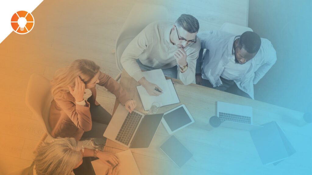 Top-down view of people gathered around a desk with laptops and papers during a Level 10 Meeting (L10).
