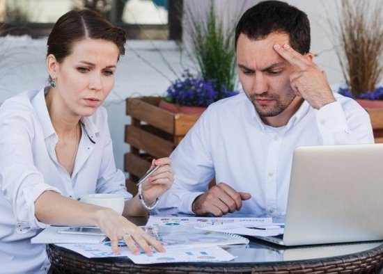 businessman and businesswoman making a decision at a table with lots of papers and a laptop