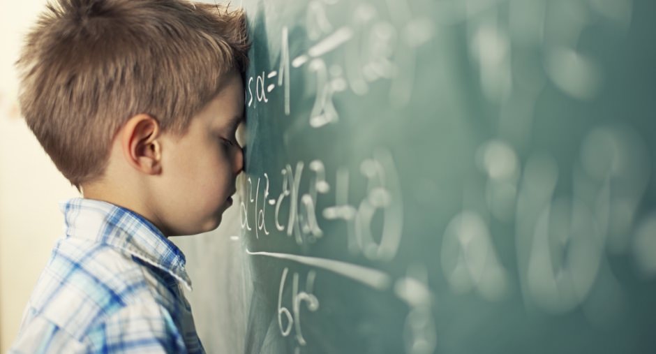 Frustrated boy resting his head on a chalkboard because his solution is the wrong one