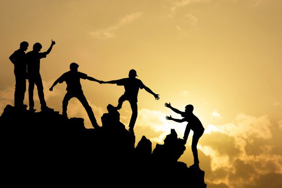 silhouetted view of people helping each other up a summit | leaving a leadership legacy