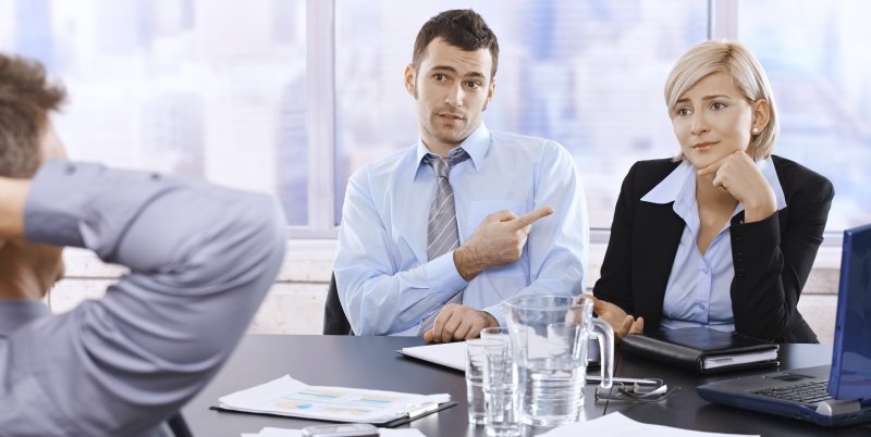 businessman pointing a blaming finger at a female colleague while sitting in a meeting