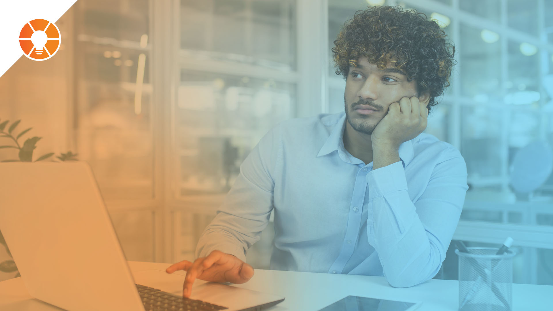 Employee sitting at a desk, looking distracted while working on a laptop in an office environment