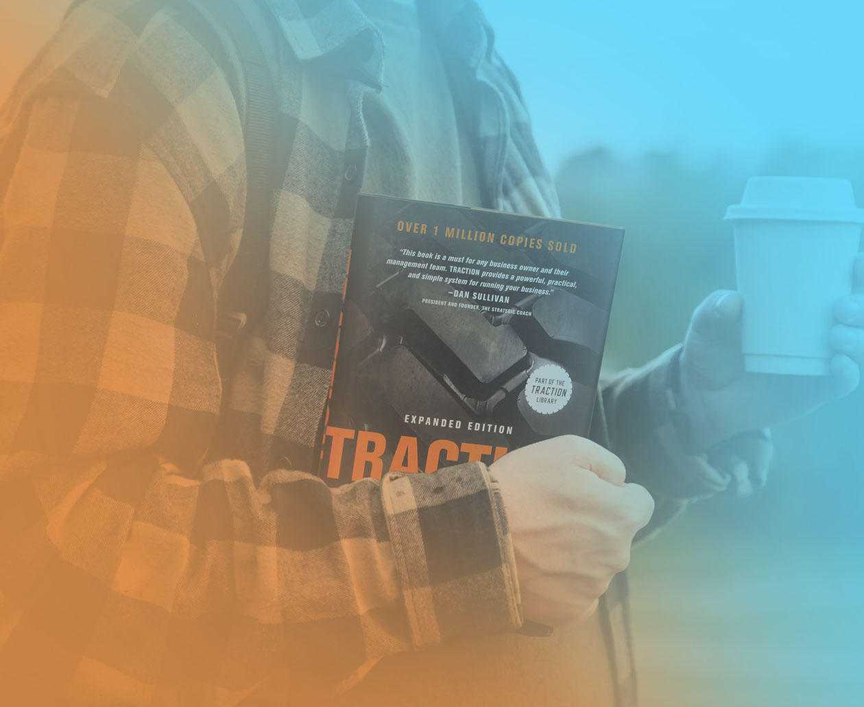 Person in a plaid flannel shirt holding a copy of the book Traction and a takeaway coffee cup, symbolizing the next steps after reading the business leadership book.